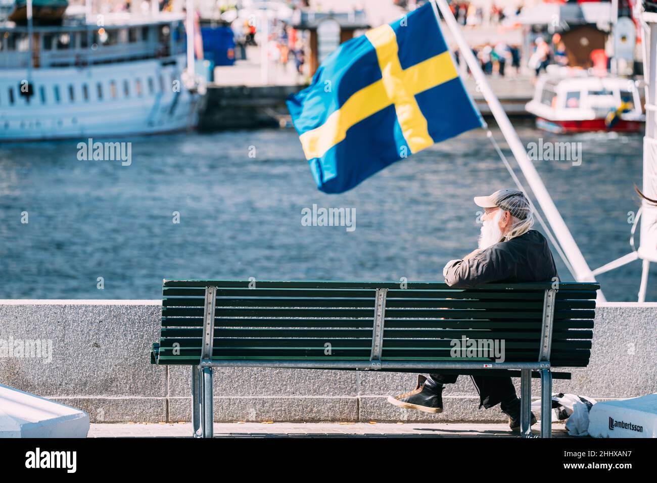 Stockholm, Suède. Old Man se trouve sur un banc près de la City Promenade. En arrière-plan UN drapeau suédois agitant. Banque D'Images
