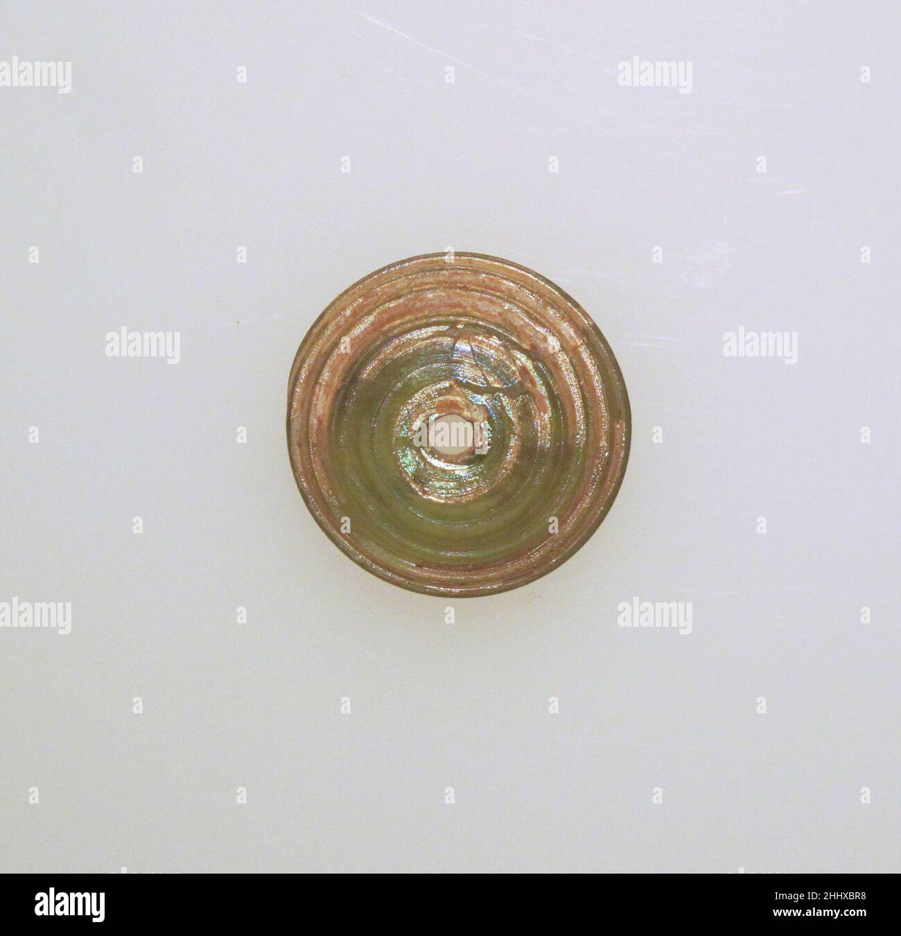 Broche en verre env.1st–2nd Century A.D. Roman translucide vert jaune clair, avec des sentiers de la même couleur.corps grand, bombé; fond légèrement convexe; trou vertical plus grand sur le fond.sentier en spirale sur la surface supérieure et le dessous.Intact; bulles de pinprick; un peu de morcellement et d'irisée crémeux.Tige en verreRomain ca.1st–2nd siècle A.D..Verre ; en forme de tige et enroulé.Du début à la mi-impériale.Verre Banque D'Images
