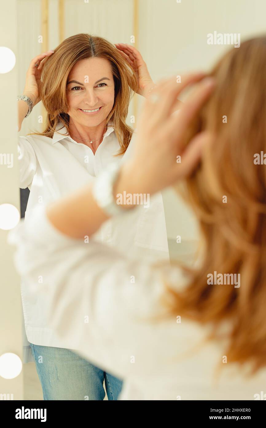 Portrait d'une belle femme souriante devant un miroir.Race blanche blonde positive.Tir vertical Banque D'Images