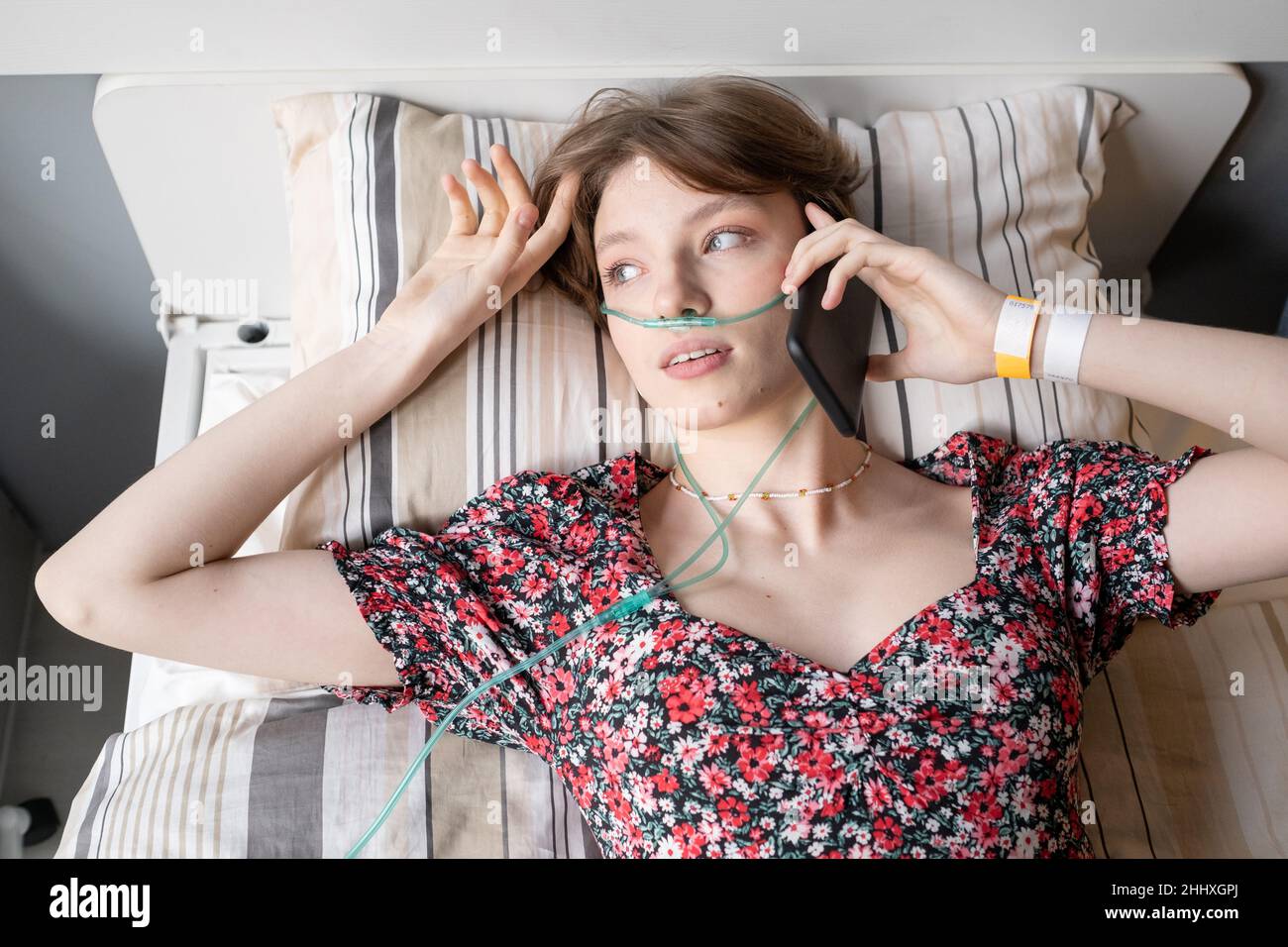 Brunette adolescente avec un tuyau d'oxygène dans le nez parlant sur un  téléphone portable tout en se reposant sur un lit dans la salle d'hôpital  Photo Stock - Alamy