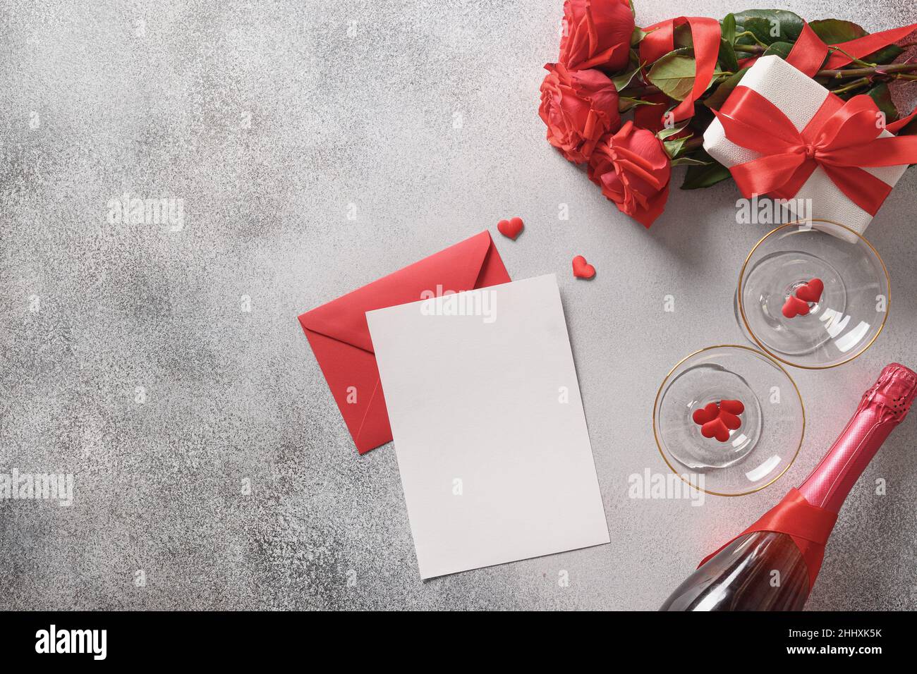 Carte de vœux de Saint-Valentin avec vide vierge pour lettre d'amour, cadeau, roses rouges, champagne et verres à vin sur fond gris.Vue de dessus.Copier Banque D'Images