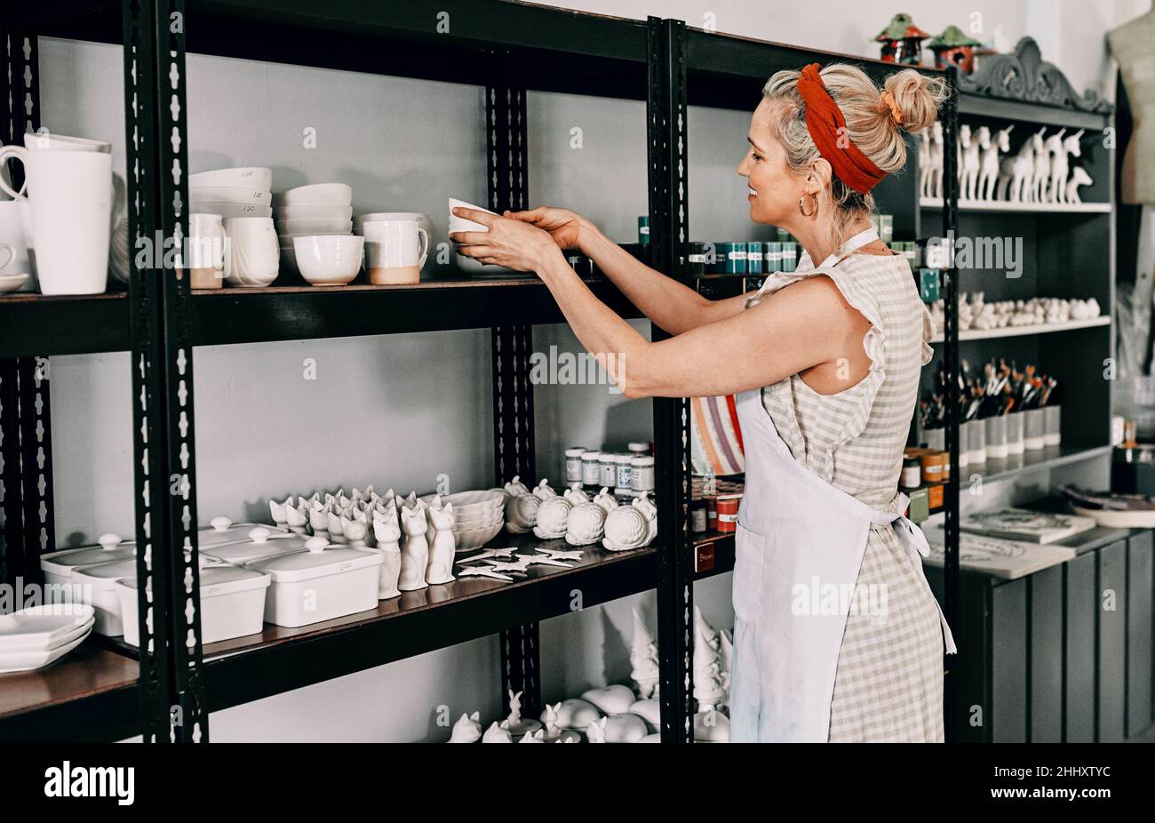 Un autre ajout à la collection.Photo rognée d'une belle femme mûre debout et organisant sa poterie sur une étagère dans son atelier. Banque D'Images