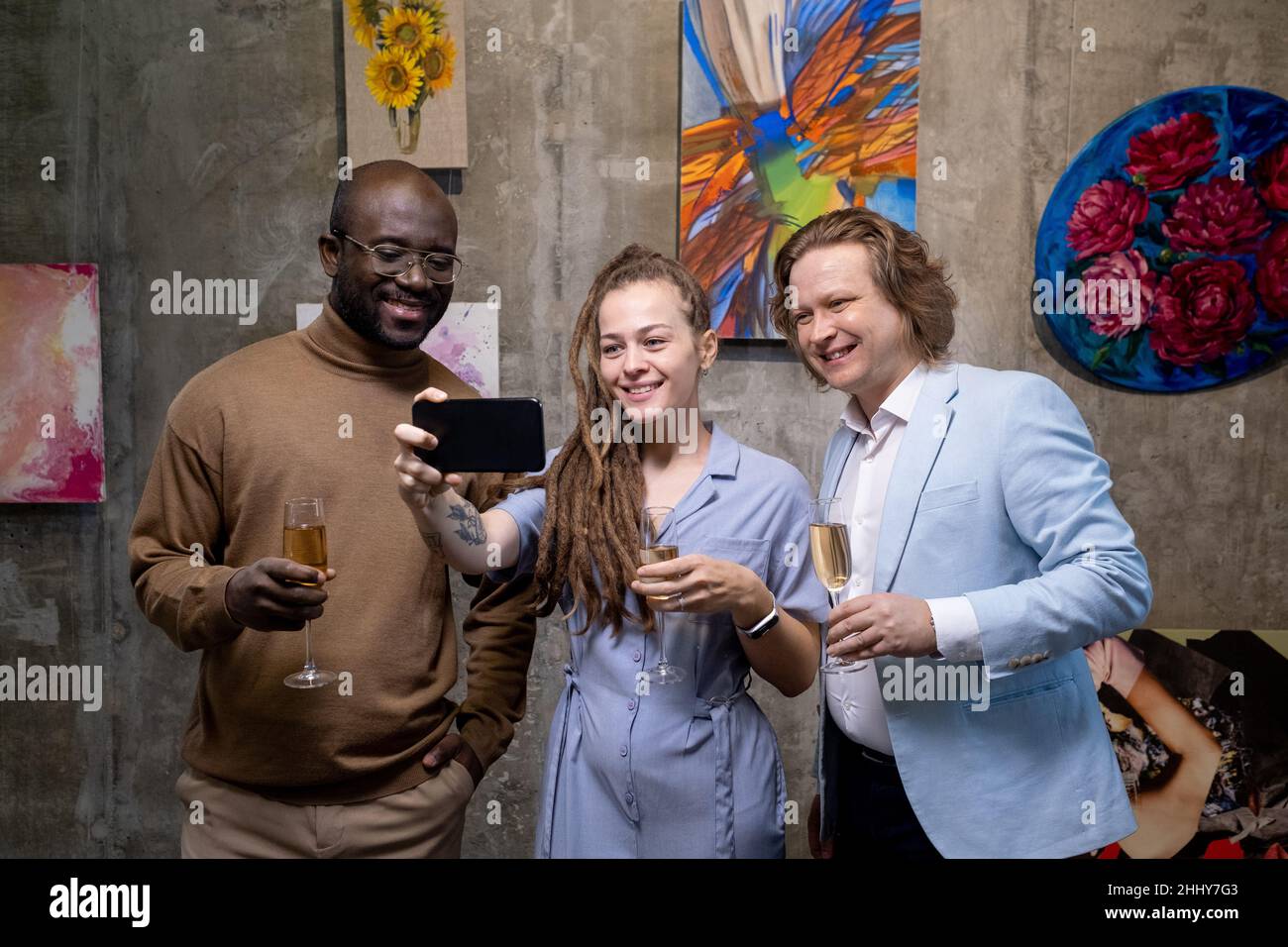 Groupe de gens heureux avec champagne faisant le portrait de selfie sur téléphone mobile contre les peintures tout en visitant l'exposition dans la galerie d'art Banque D'Images