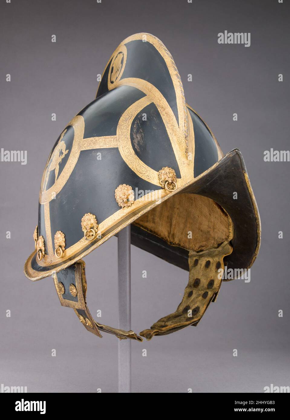 Morion ca.1600 Allemand, Nuremberg forgé en une seule pièce ce casque est doté d'un grand sabot sur son bol arrondi et d'une élégante visière portée jusqu'aux points les plus pointus à l'avant et à l'arrière.Les cheekpieces avec mentonnières sont construites à partir de trois plaques superposées.Les têtes décoratives des rivets fixant la doublure sont des masques de lion qui maintiennent des anneaux dans leur bouche; les têtes de rivets sur les pièces de joue sont des rosettes en laiton.Un porte-panache en laiton en forme de demi-figurine femelle à ailettes est fixé à l'extrémité arrière du peigne.Toute la surface est noircie sauf pour les bandes gravées et dorées des arabesques al Banque D'Images