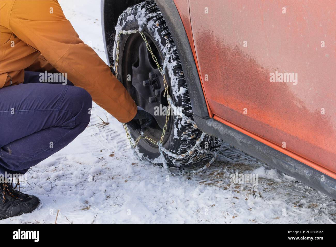 Le conducteur installe des chaînes sur le volant de sa voiture orange en hiver.Équipement du véhicule pour la conduite hors route et par mauvais temps. Banque D'Images