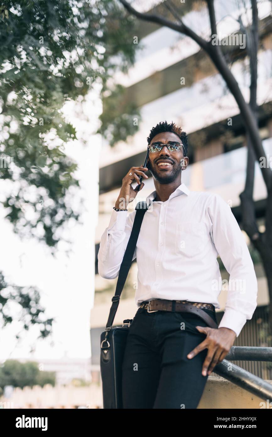 Jeune homme d'affaires noir souriant parlant sur son téléphone dans la rue en portrait Banque D'Images
