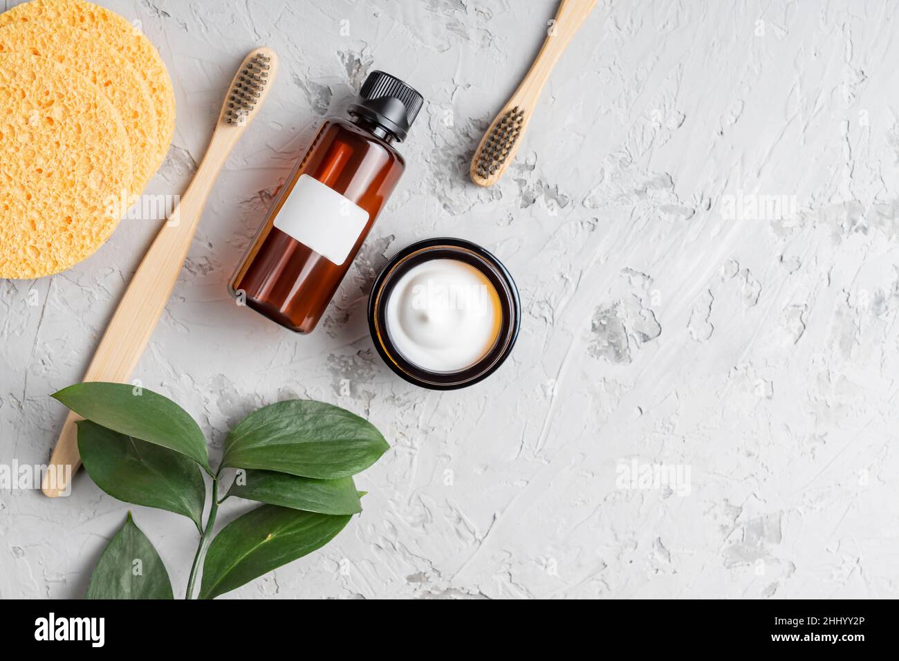 outils d'hygiène personnelle et cosmétiques sur fond de béton avec espace de copie.Crème visage et essence en verre jae, brosses à dents en bambou écologiques an Banque D'Images