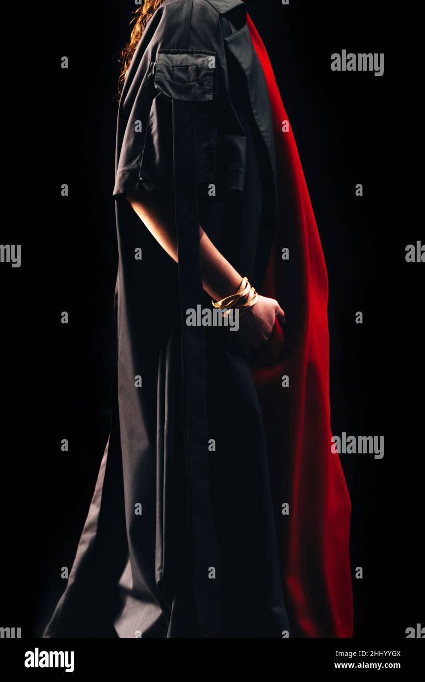 Modèle court de mode portant un long manteau noir et une robe marchant sur la piste sur fond noir.Détails fantaisie.Mode féminine Banque D'Images
