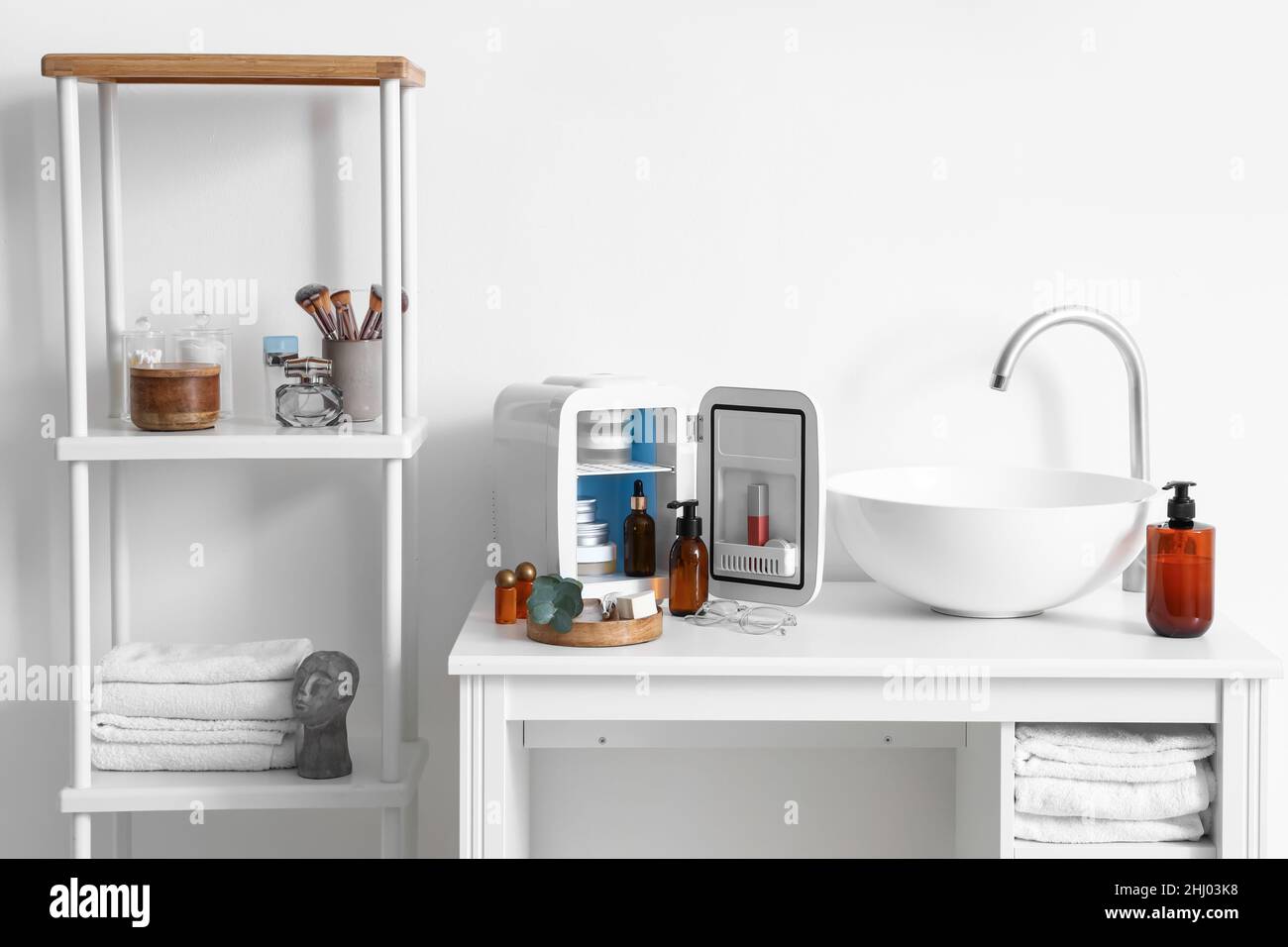 Évier, réfrigérateur ouvert et produits cosmétiques sur la table près du mur lumineux dans la salle de bains Banque D'Images