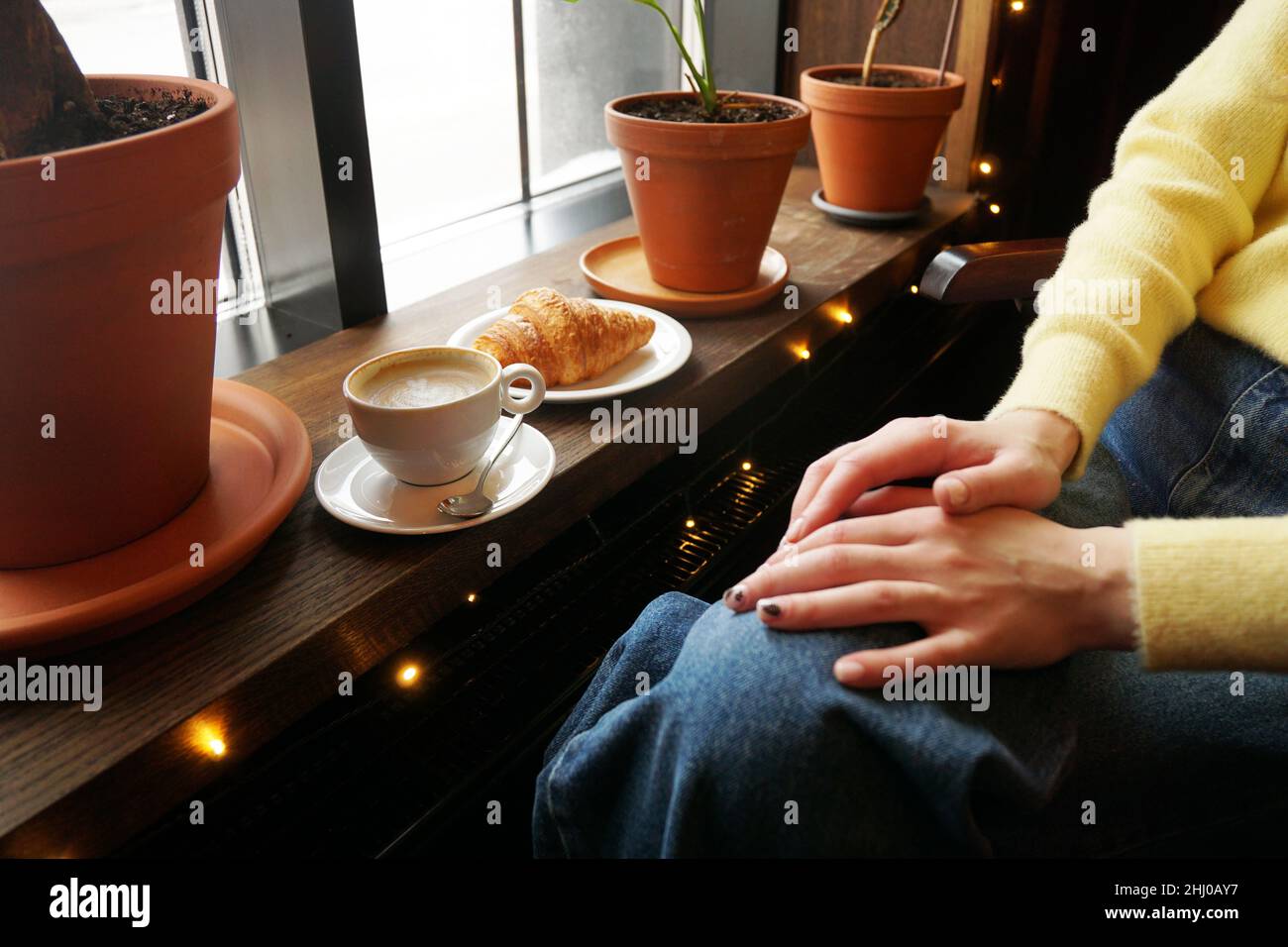 Service simple de cappuccino avec art floral en forme de cœur sur une table en bois sombre.Jean bleu d'une fille assise dans un café Banque D'Images