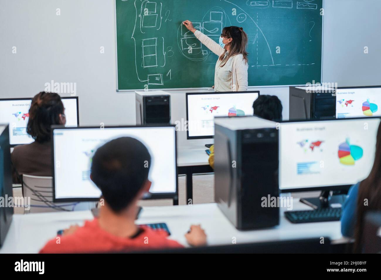 Élèves multiraciaux utilisant des ordinateurs pendant la classe d'affaires portant des masques de sécurité à l'école - accent sur l'enseignant Banque D'Images