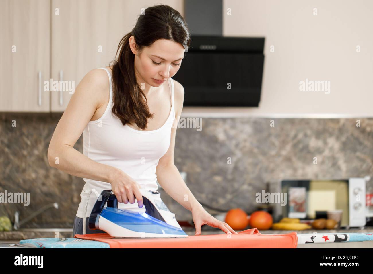 Travaux ménagers de routine. Une femme reporte ses vêtements avec un fer à repasser. Sur le fond de l'appartement Banque D'Images