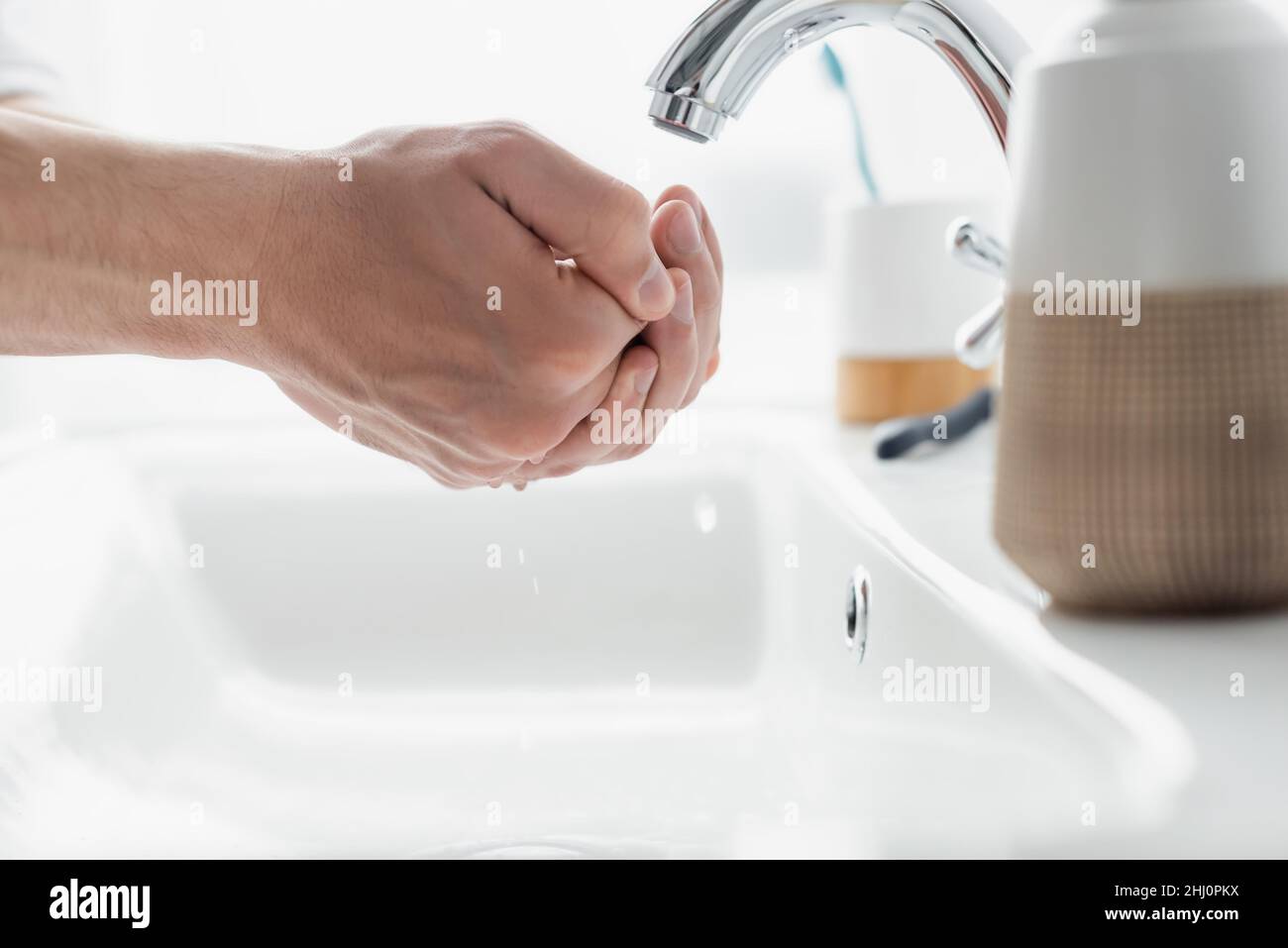 vue rapprochée des mains mâles près du robinet et des articles de toilette flous Banque D'Images