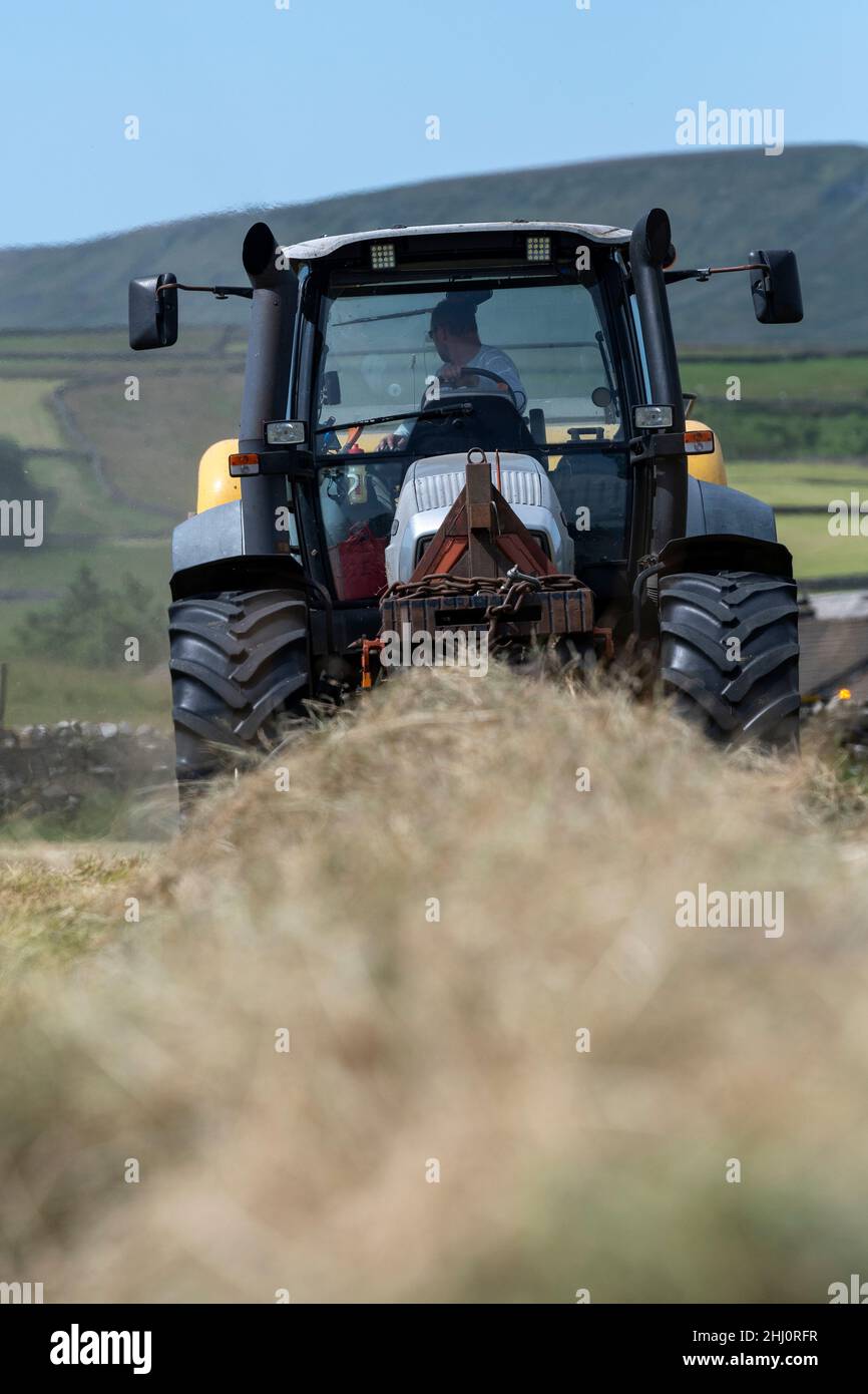 Exploitant agricole qui fait du foin de prairie traditionnel sur les hautes terres, avec un tracteur Hurlimann XL et une presse à balles carrées haute densité New Holland BB9060.Hawes, Yorkshire du Nord, U Banque D'Images