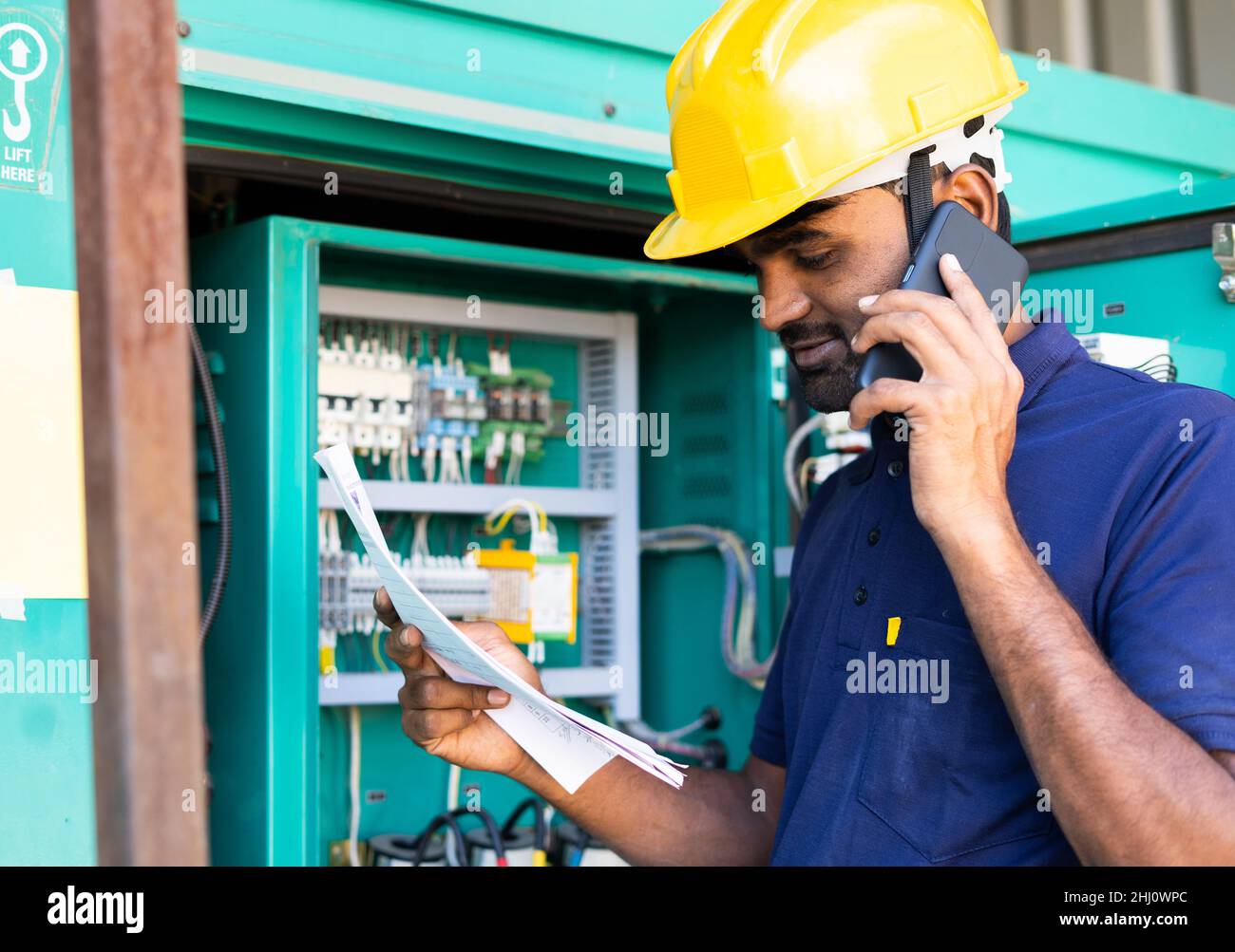 un électricien lit ou inspecte en parlant avec un collègue sur un téléphone portable devant la carte de circuit imprimé - concept de travail d'équipe, de réparation ou Banque D'Images