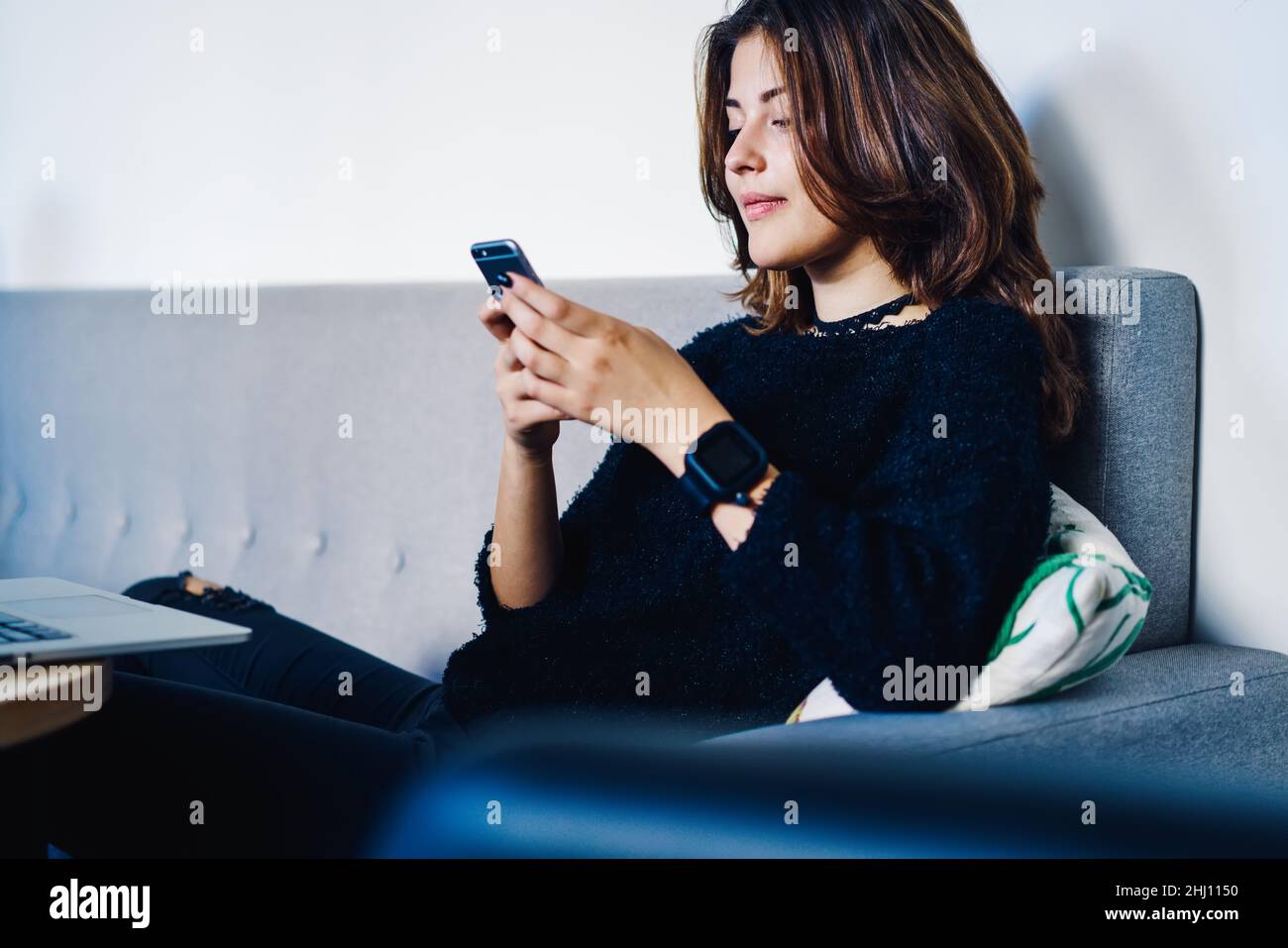 Femme parcourant un téléphone portable assis sur un canapé Banque D'Images