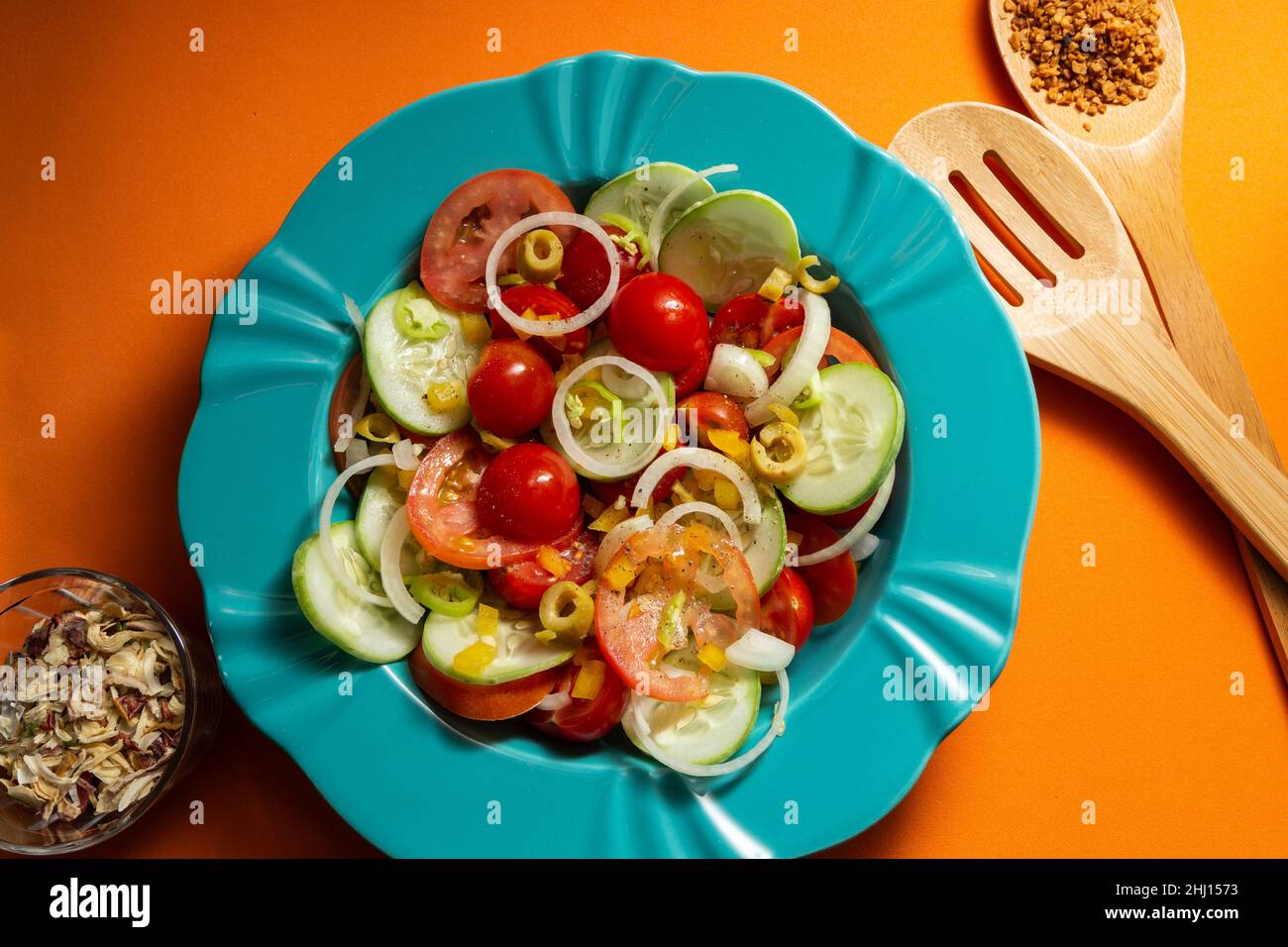 Goiania, Goias, Brésil – 25 janvier 2021 : une assiette de salade de légumes, un verre aux épices déshydratées et deux couverts en bois sur fond orange Banque D'Images