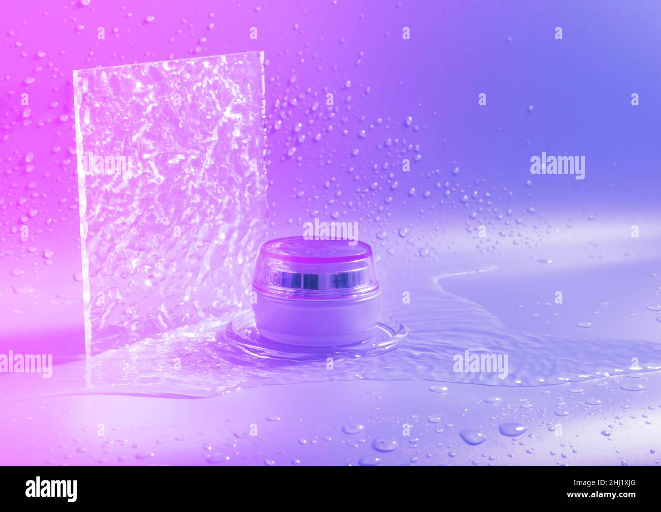 Crème cosmétique dans un pot, éclaboussures et gouttes d'eau sur fond violet dégradé.Soins du visage, du corps, des cheveux Banque D'Images
