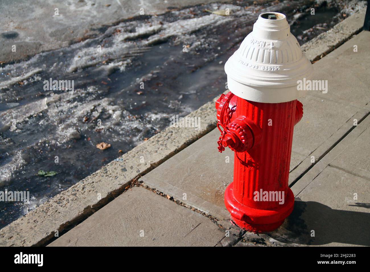 Une vieille borne d'eau traditionnelle rouge et blanche avec de la glace et de la neige sur le sol par une journée ensoleillée en hiver Banque D'Images