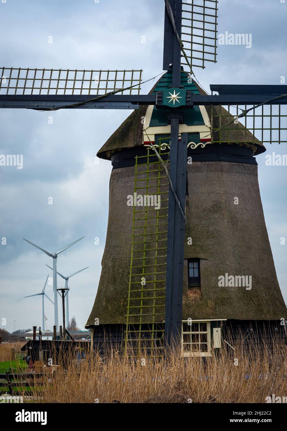 Moulin historique hollandais devant les éoliennes modernes, comparaison des technologies anciennes et nouvelles Banque D'Images