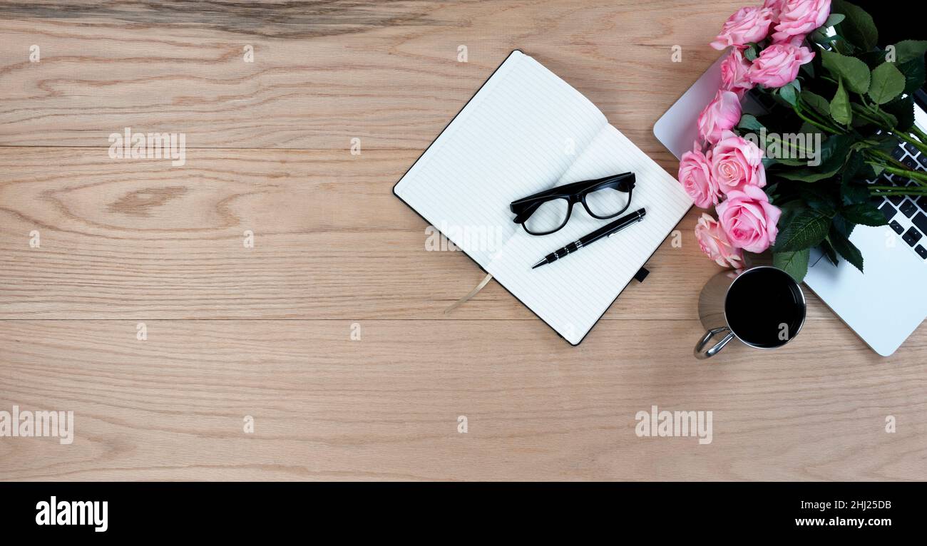 Bureau en bois de chêne table avec de jolies roses roses, ordinateur portable, matériel d'écriture et boisson de café pour les mères cadeau de jour au travail ou à l'école. Banque D'Images