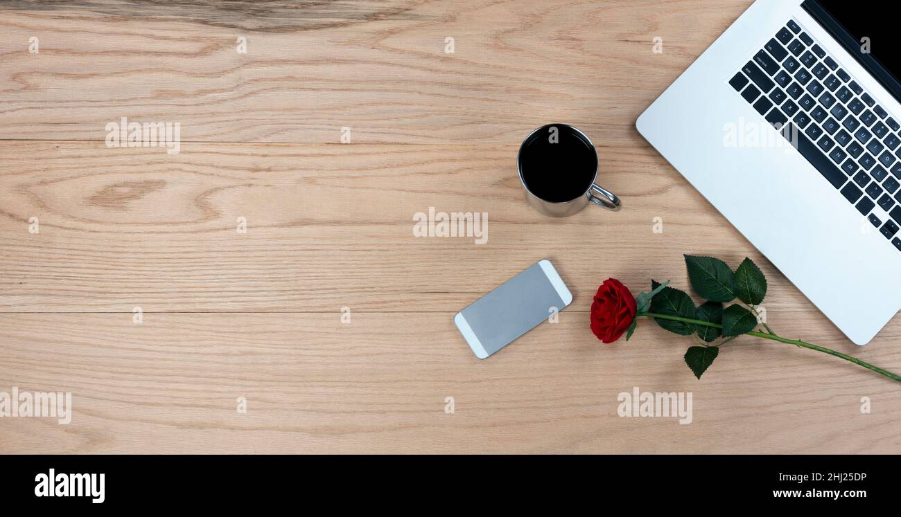 Bureau en chêne, table avec rose rouge, tasse de café, smartphone et ordinateur portable pour un cadeau de la Saint Valentin au travail ou à l'école. Banque D'Images