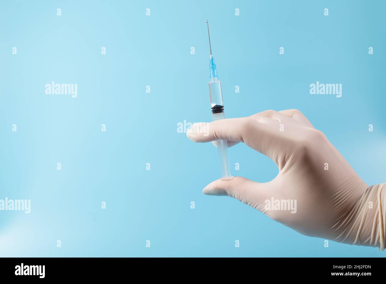 Les mains du médecin dans des gants blancs tenant la seringue avec le vaccin, gros plan sur fond bleu avec la sapce de copie. Banque D'Images