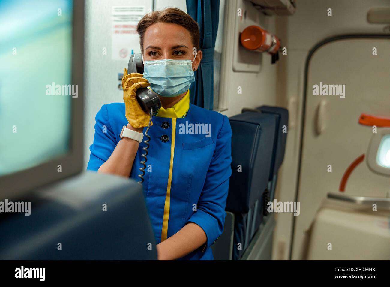 Hôtesse dans un masque médical utilisant le téléphone dans la cabine de l'avion Banque D'Images