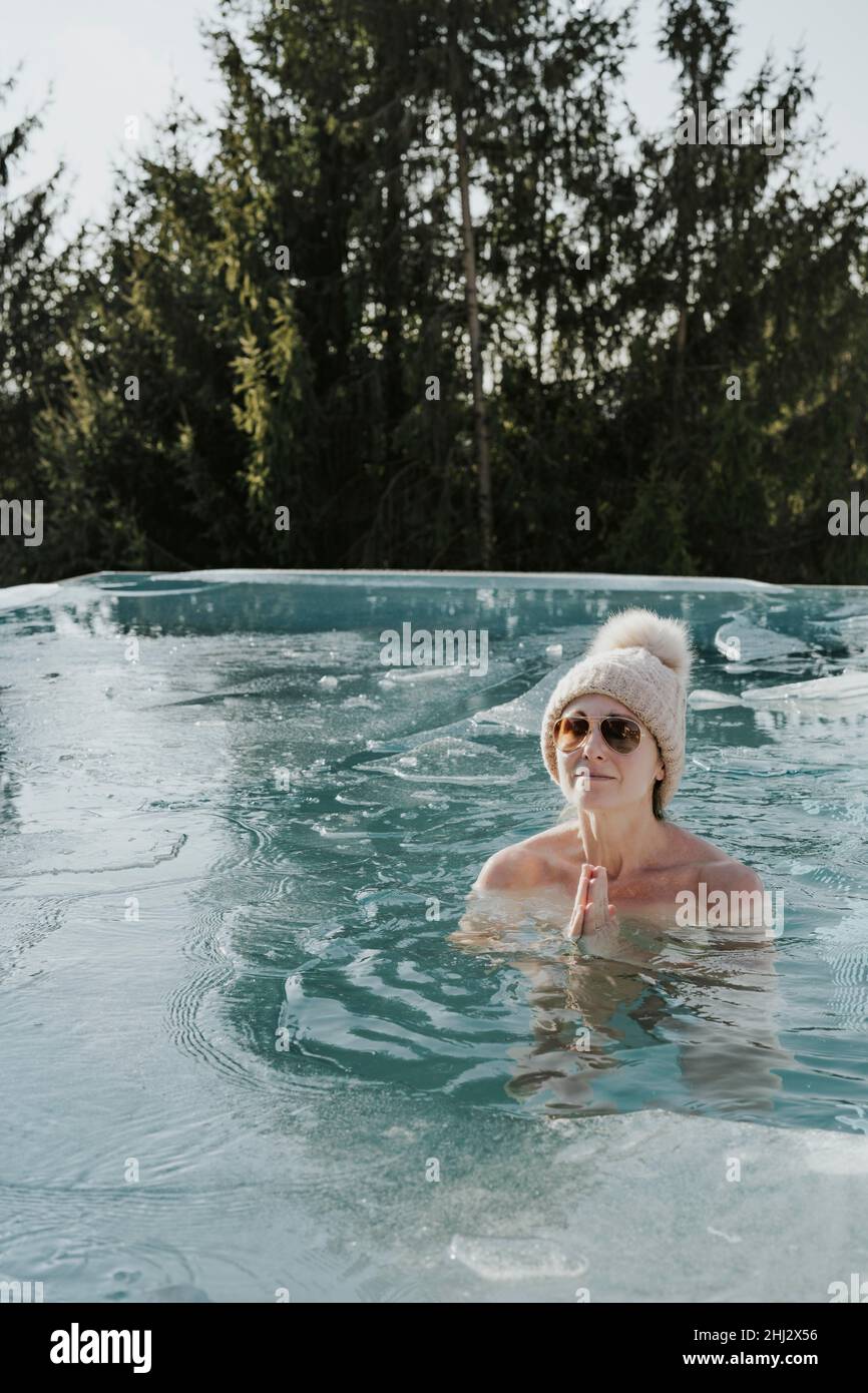Femme en casquette replie les mains pendant le bain de glace dans la piscine Banque D'Images