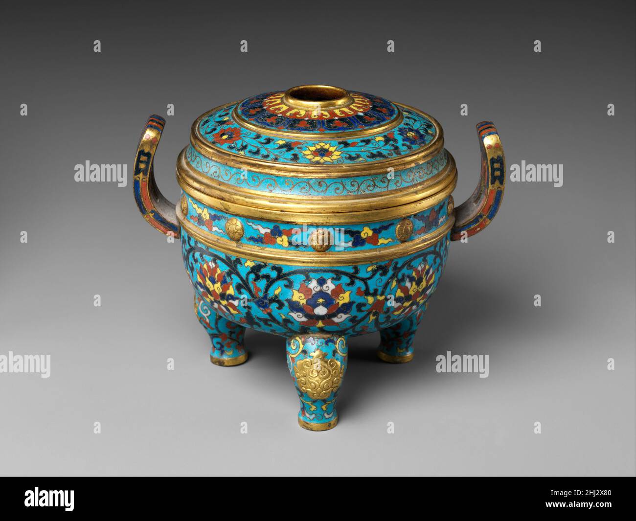 Tripode brûleur d'encens avec couvercle début du 15th siècle l'émail de la Chine cloisonné a été introduit en Chine de l'Ouest pendant le XIVe siècle.La technique a été utilisée en Chine pour créer des conceptions sur des récipients métalliques, généralement en alliage de cuivre, en plaçant de la pâte de verre coloré dans des boîtiers formés par des fils de cuivre.Depuis le XVe siècle, le cloisonné a été grandement apprécié par la cour impériale de Ming pour ses couleurs vives et son design complexe.Les artistes chinois l'ont employé pour des formes et des motifs traditionnels, tels que ce brûleur à encens en forme d'un ancien trépied en bronze décoré avec des voluées de lotus Banque D'Images