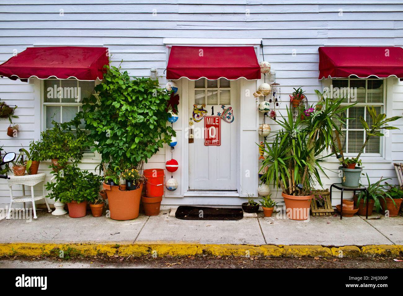 Porte avant avec marqueur de distance “0” et geckos décoratifs à Key West, Floride, FL, États-Unis.Des bouées de pêche suspendues et un auvent rouge entourent la porte. Banque D'Images