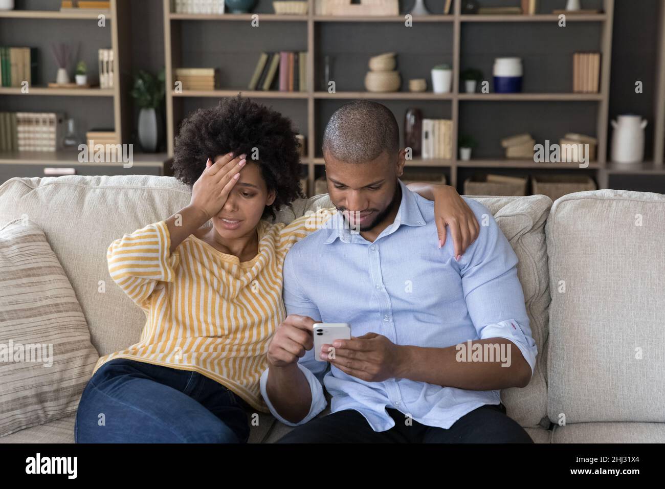 La femme africaine agacée se sent insatisfaite de la dépendance de smartphone de mari Banque D'Images