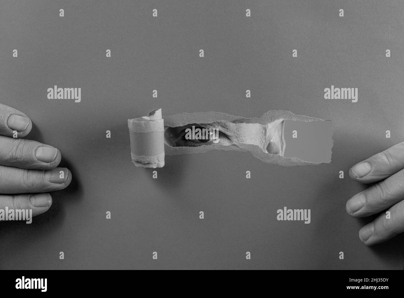 l'œil d'un homme regardant à travers la déchirure dans une feuille de papier Banque D'Images