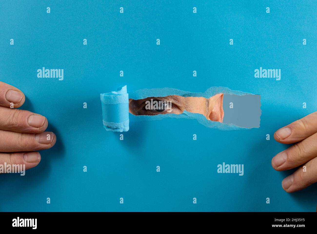 l'œil d'un homme regardant à travers la déchirure dans une feuille de papier Banque D'Images