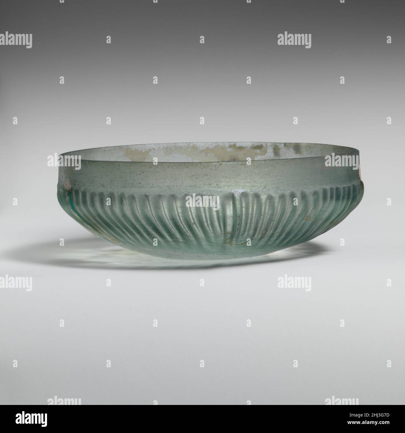 Bol en verre nervuré fin du 1st siècle C.-B.–mi-1st siècle A.D. Roman bleu translucide vert.rebord vertical avec bord supérieur angulaire;Bande plate et verticale autour du haut des côtés, puis renflée vers l'extérieur avant de couronner fortement vers le bas légèrement concave.à l'intérieur, trois fines rainures concentriques autour du bord extérieur du bas et un petit cercle plus large au centre;À l'extérieur, soixante-dix côtes verticales ou légèrement obliques de longueur, largeur et épaisseur légèrement variables, avec des sommets meulées, disposées autour de la section centrale du corps. Intact; bulles de piqûre, morcellement et iridescenence avec petites Banque D'Images