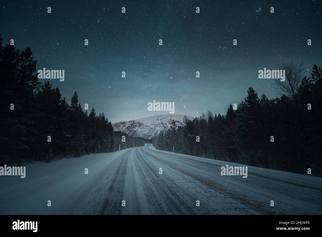 Une route de nuit et de beaux paysages avec ciel étoilé.Paysage d'hiver avec route vide, forêt et montagnes. Banque D'Images