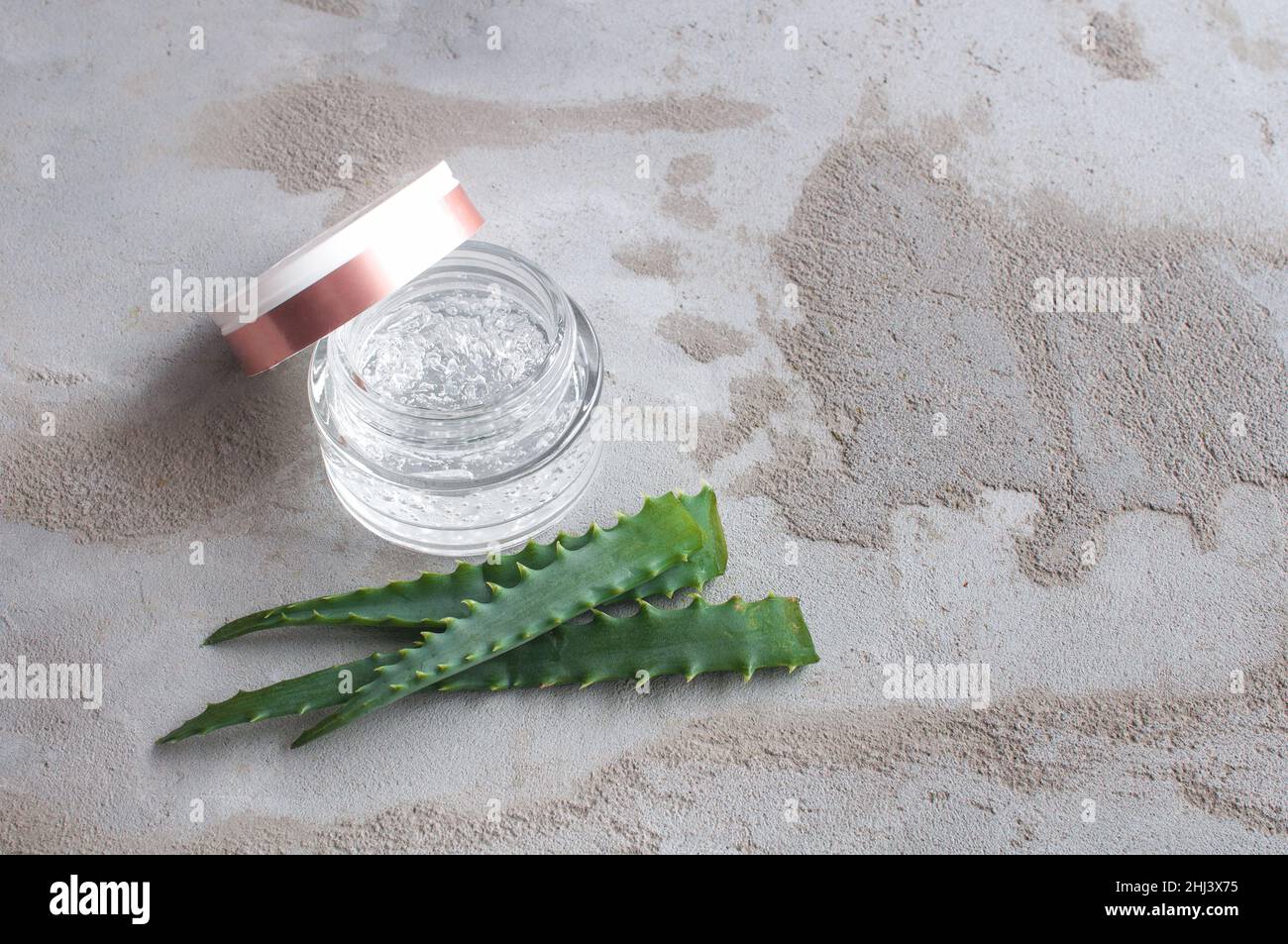 Texture de gel avec des bulles d'acide hyaluronique et des branches d'aloe vera dans un pot de verre sur un fond de béton Banque D'Images