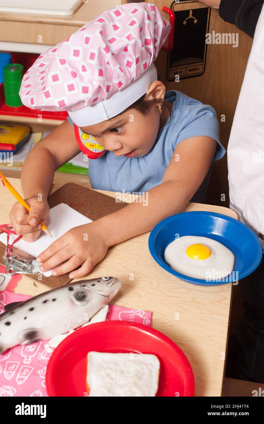 Éducation préscolaire 4 ans prétendre jouer fille chef écrire la commande de nourriture jouet téléphone à l'oreille Banque D'Images