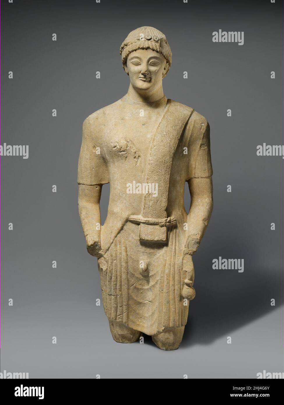 Statue en calcaire d'un votaire mâle première moitié du 5th siècle avant  J.-C. chypriote la figure porte un aryballos (une petite bouteille d'huile)  dans sa main gauche et porte une gaine d'épée
