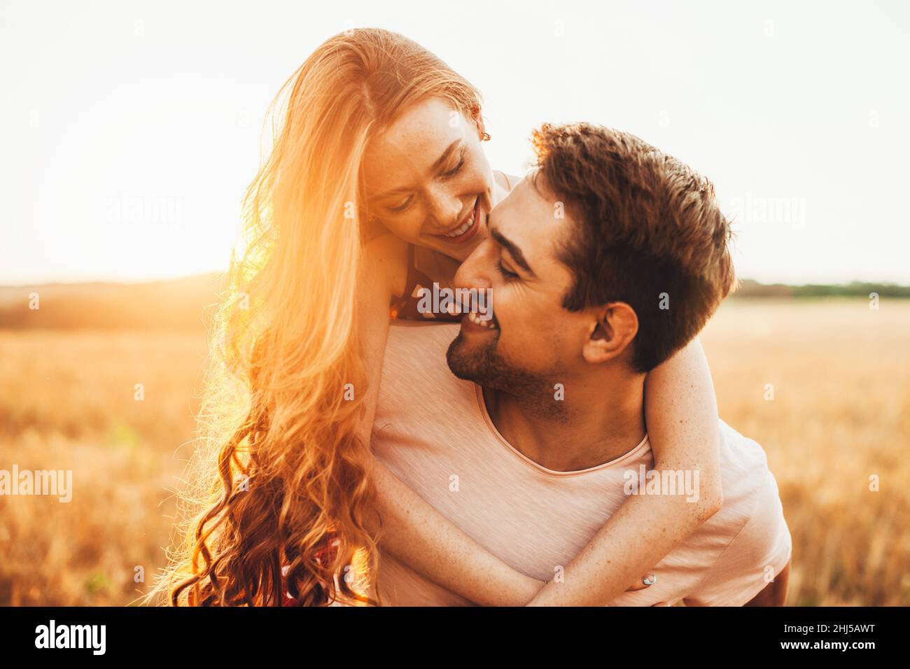 Portrait en gros plan d'une fille aux cheveux rouges avec un visage défoncé debout derrière son mari et embrassant son cou au soleil.Pour un style de vie Banque D'Images