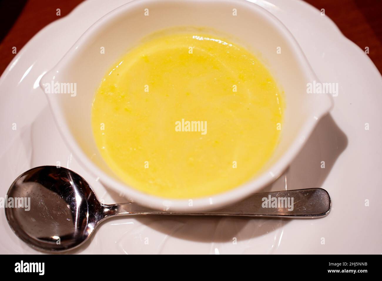 Un petit bol blanc élégant de soupe de maïs jaune doux fait de maïs de marque de Hokkaido Japon avec une cuillère ronde en métal et une assiette blanche en dessous Banque D'Images