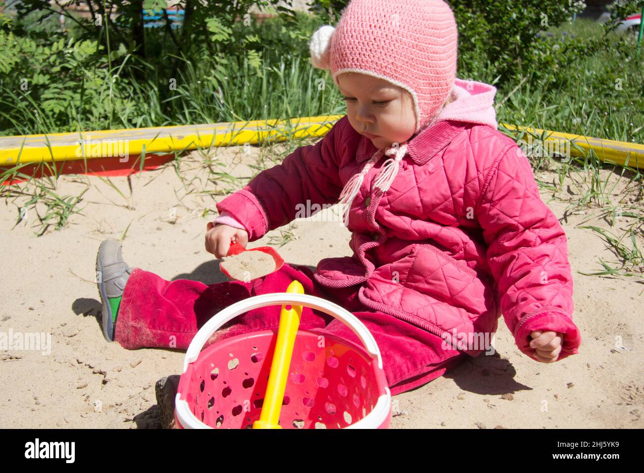 Enfant de deux ans jouant avec du sable et une pelle dans un bac à sable sur l'aire de jeux Banque D'Images