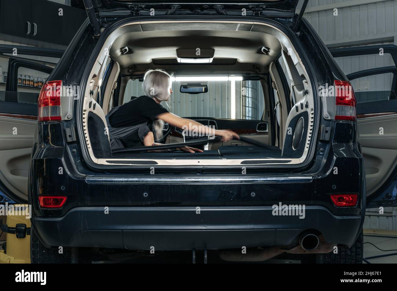 Femme travailleuse aspirant poussière intérieur de la voiture dans le lave-auto. Banque D'Images