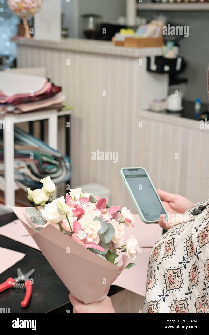 fleuriste dans un fleuriste tenant un bouquet et textant à un client. petite entreprise, livraison de fleurs, espace de travail Banque D'Images