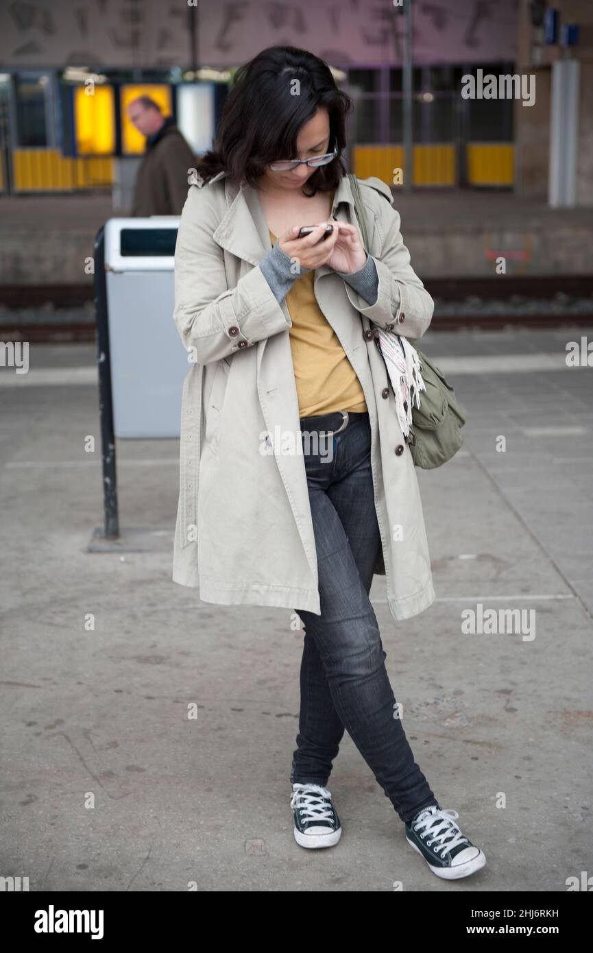 Rotterdam, pays-Bas. Une jeune femme adulte tue du temps en vérifiant des messages sur son smartphone tout en attendant son train Intercity à la gare centrale de la ville. Banque D'Images
