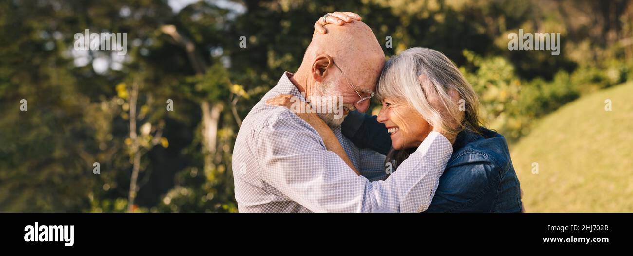 Couple âgé se touchant la tête en se tenant debout à l'extérieur.Couple senior heureux partageant un moment romantique dans un parc.Couple d'âge mûr et gai Banque D'Images