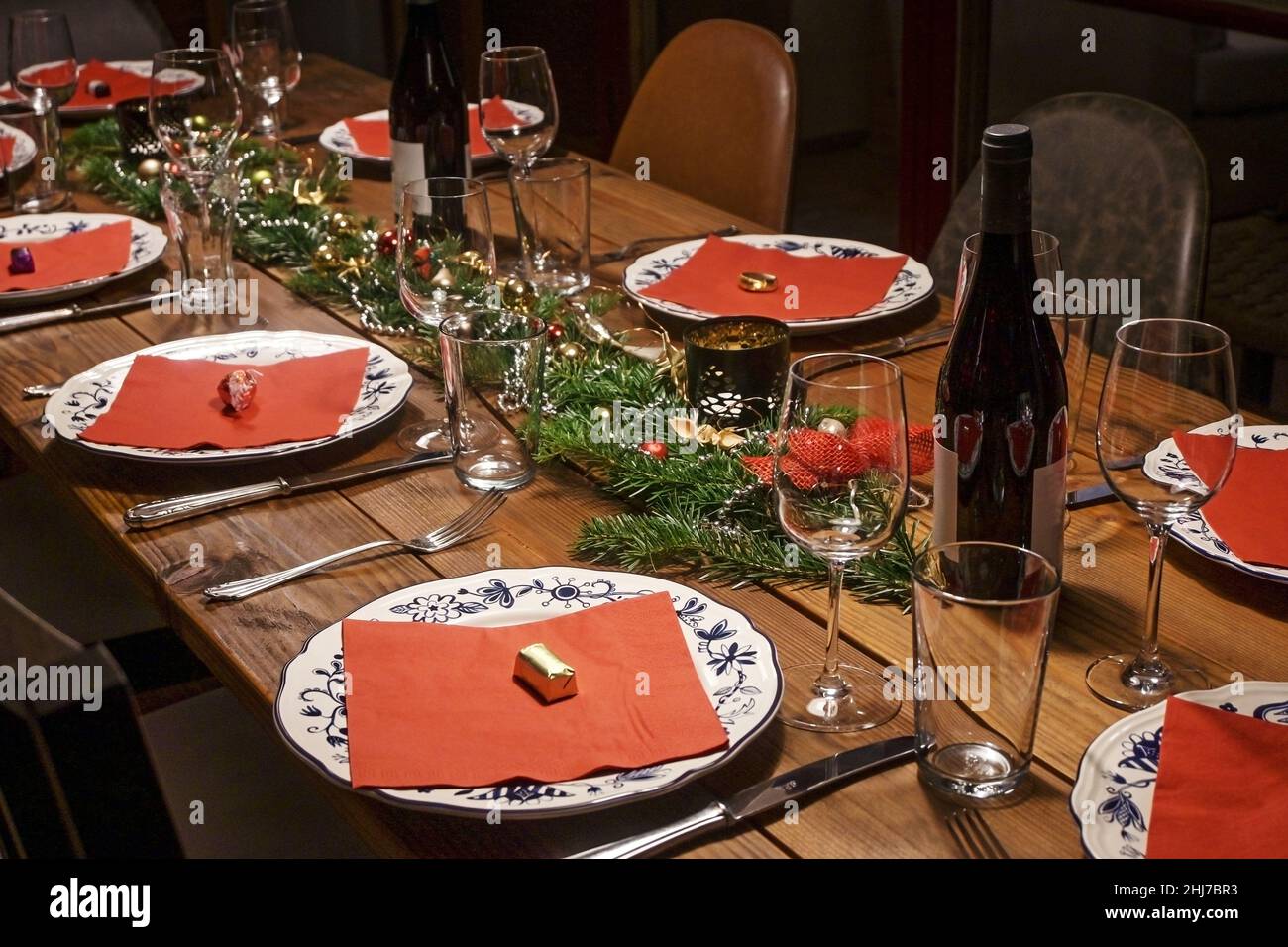 Grande table rustique en bois décor festif et décoré pour un dîner entre amis ou en famille, assiettes à motifs blanches, serviettes rouges, vin et verres, sélection Banque D'Images