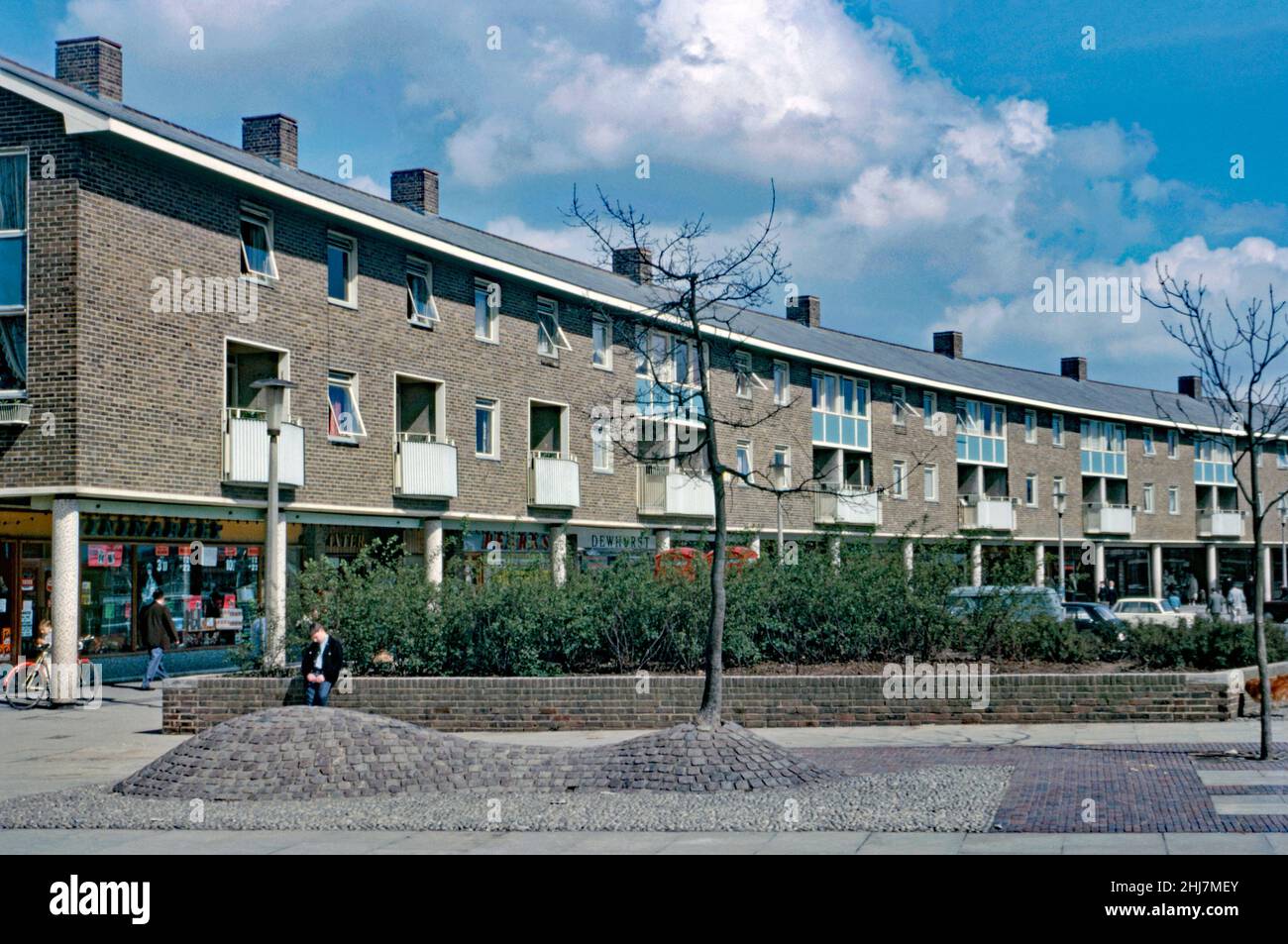 Nouveaux magasins et appartements (maisonnettes) ci-dessus à Tilgate Parade, Ashdown Drive dans la zone de Tilgate de Crawley 'New Town', West Sussex, Angleterre, Royaume-Uni en 1966.Le quartier, au sud du centre-ville, était l'une des 14 banlieues développées pour créer la nouvelle ville d'après-guerre.La parade à la façade de briques a une forme légèrement courbée.Après la Seconde Guerre mondiale, afin de relocaliser ceux qui vivent dans des logements pauvres ou bombardés à Londres, un grand nombre de personnes et d’emplois ont été transférés dans de nouvelles villes autour de la se Angleterre et Crawley en était une.Cette image est tirée d'une ancienne transparence de couleur amateur – une photographie vintage 1960s. Banque D'Images