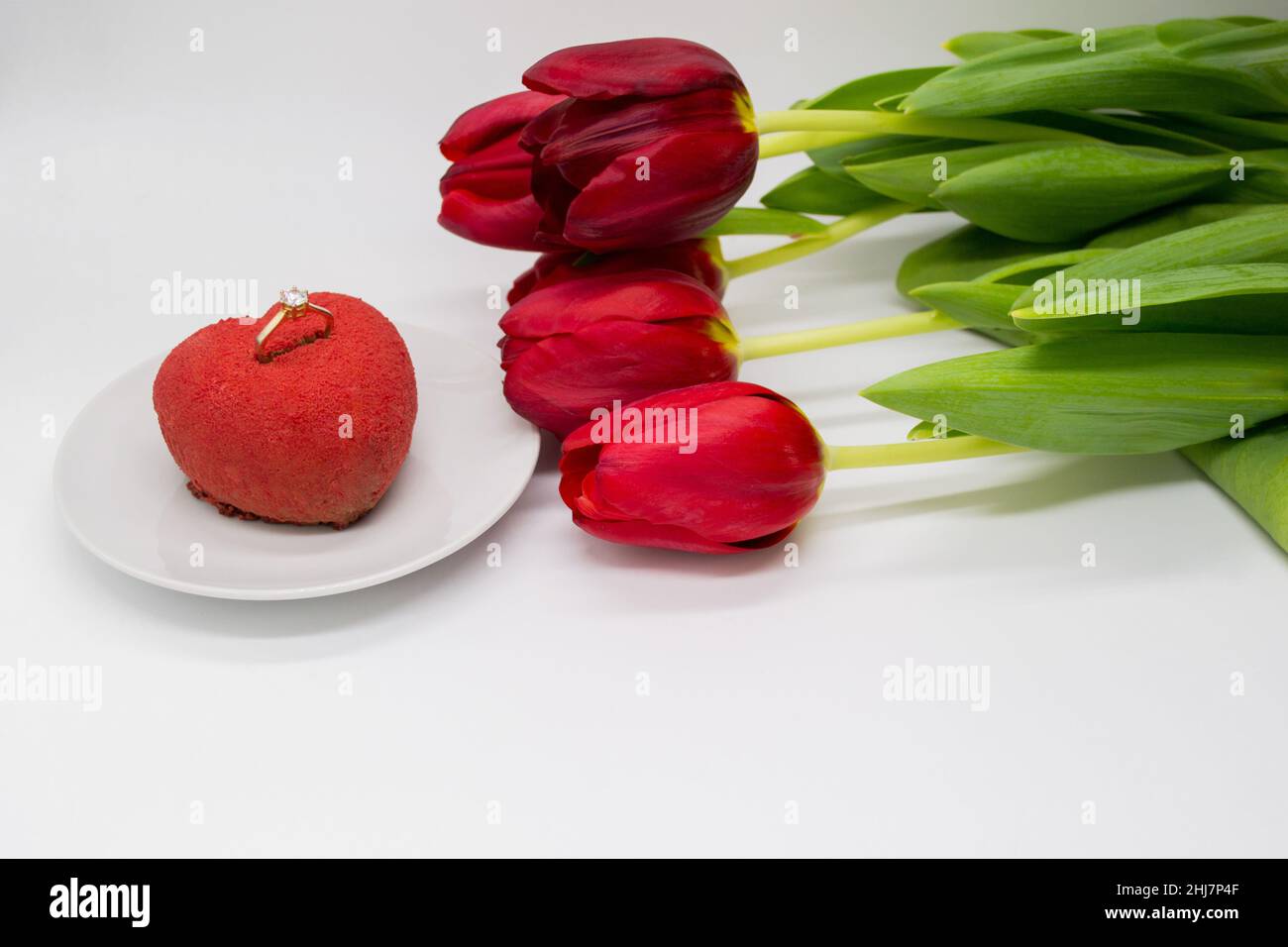 Un bouquet de tulipes rouges à côté d'une assiette avec un gâteau en forme de coeur, dans lequel un anneau d'or avec un diamant. Banque D'Images