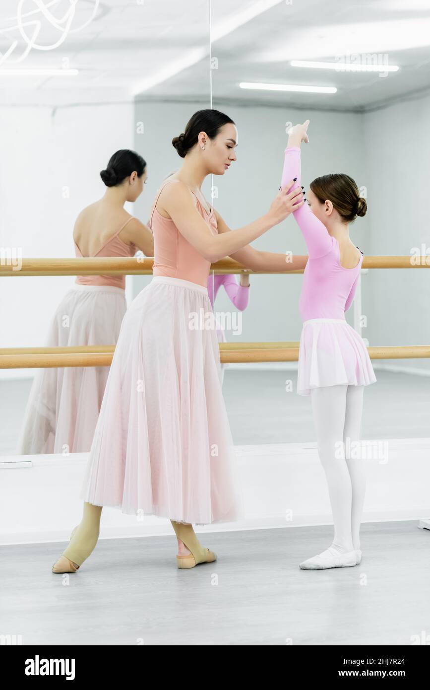 vue en longueur du maître de ballet levant la main de fille près de barre et miroirs dans le studio Banque D'Images